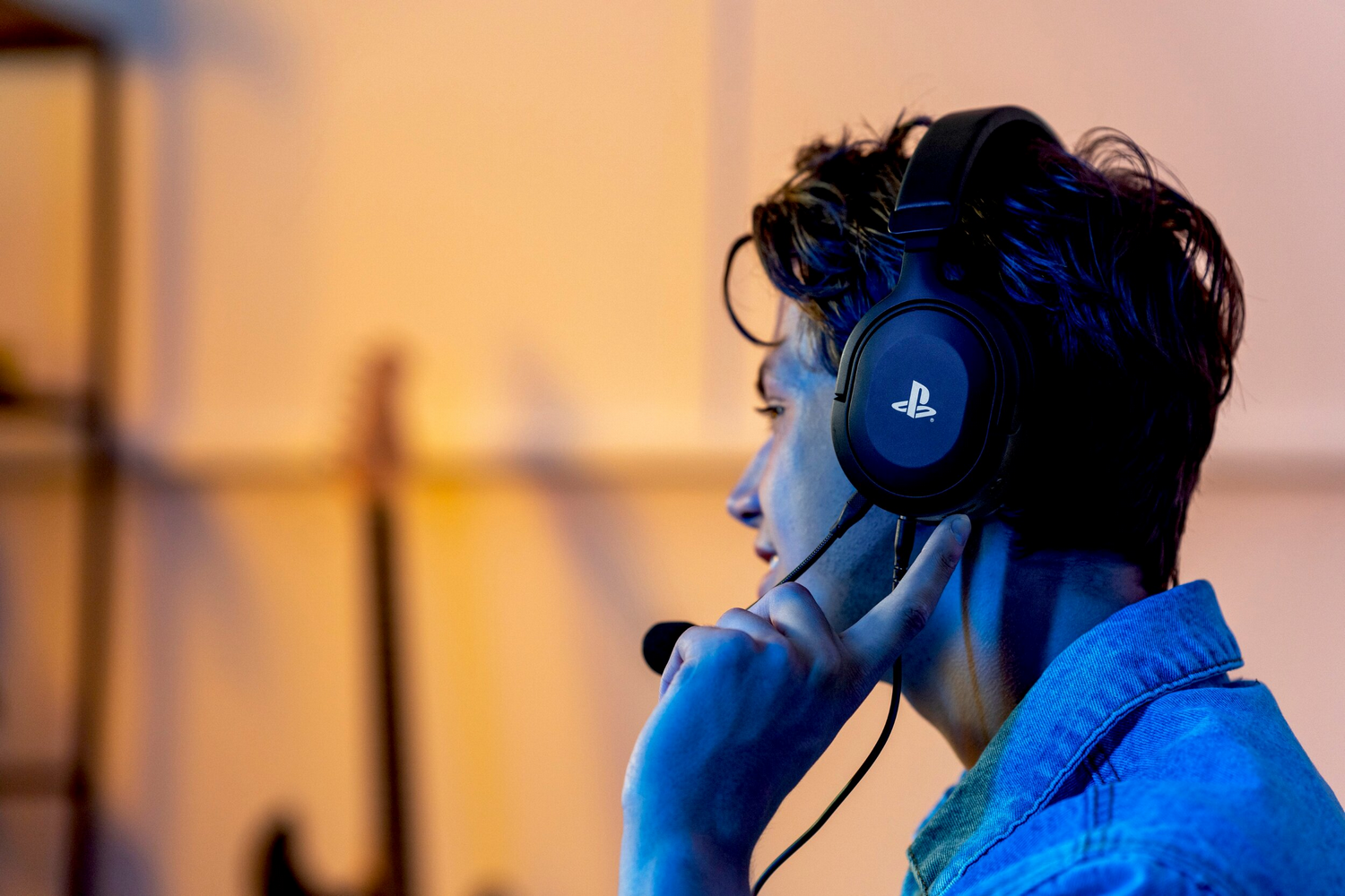 Un hombre joven con auriculares y micrófono, de perfil, con camisa azul.