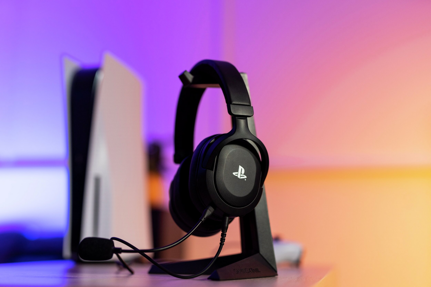 Auriculares negros con micrófono en un soporte, junto a una consola de juegos.
