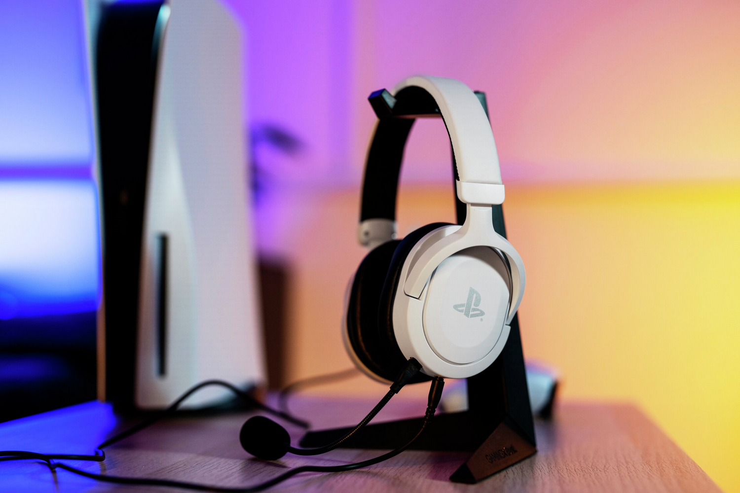 Unos auriculares blancos con logo de PlayStation en un soporte junto a una consola.