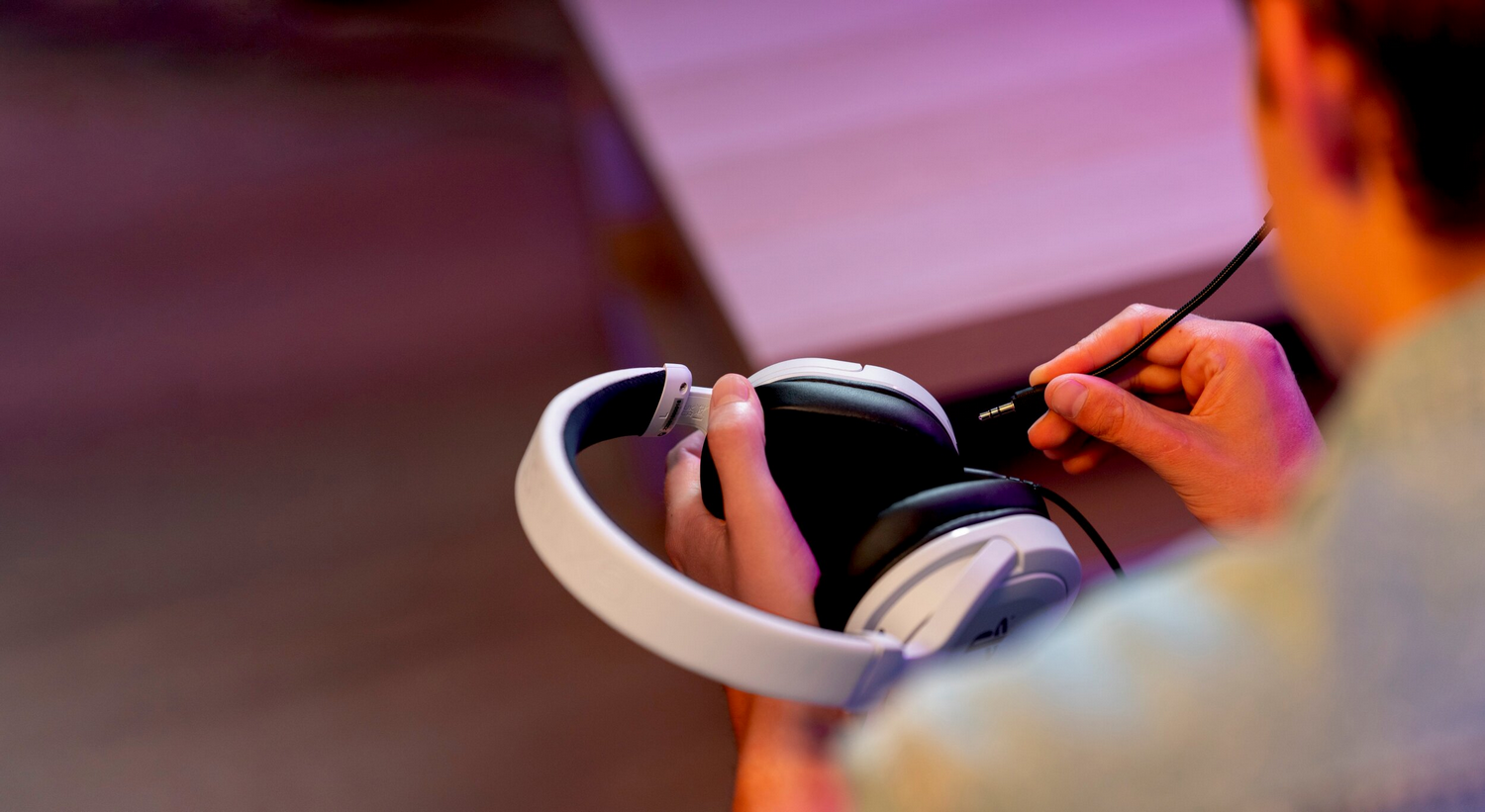 Una mano sujeta auriculares blancos con almohadillas negras, enchufando un cable.