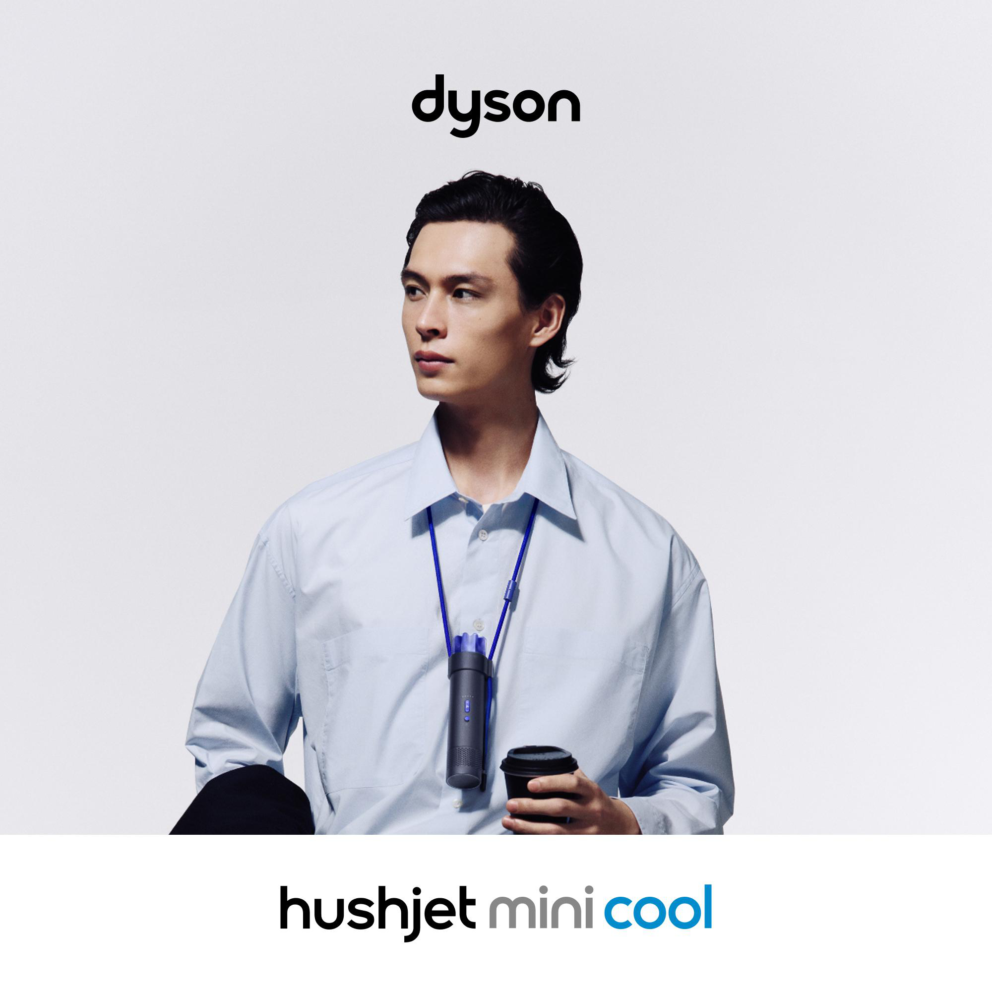 Ein Mann mit hellblauem Hemd hält eine Kaffeetasse und trägt einen Dyson Luftkühler.