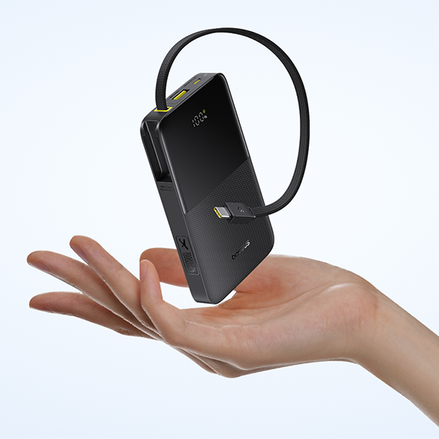 Una mano sostiene un cargador portátil negro con cable USB-C, mostrando 100%.