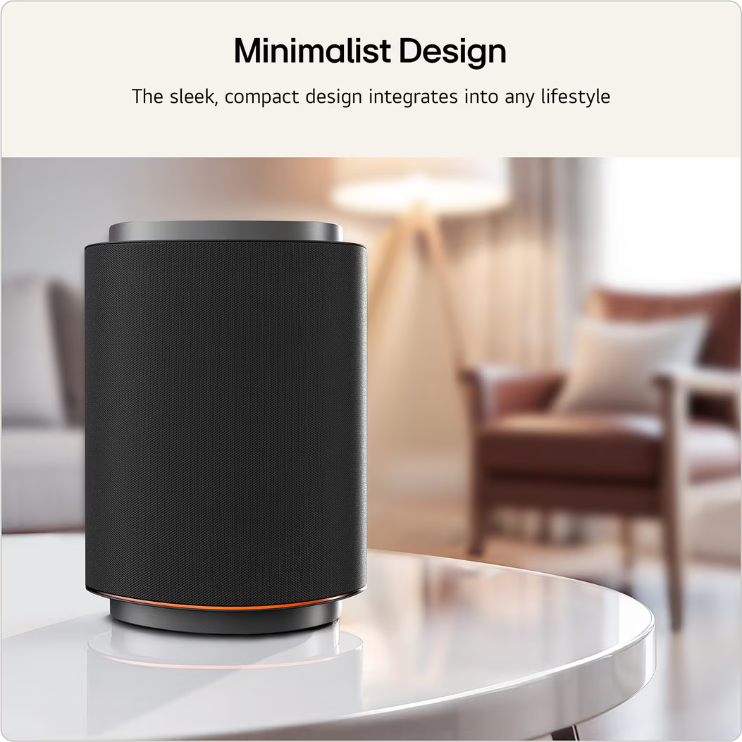 Une enceinte cylindrique noire avec un dessus argenté est sur une table blanche. Un anneau lumineux orange est visible.