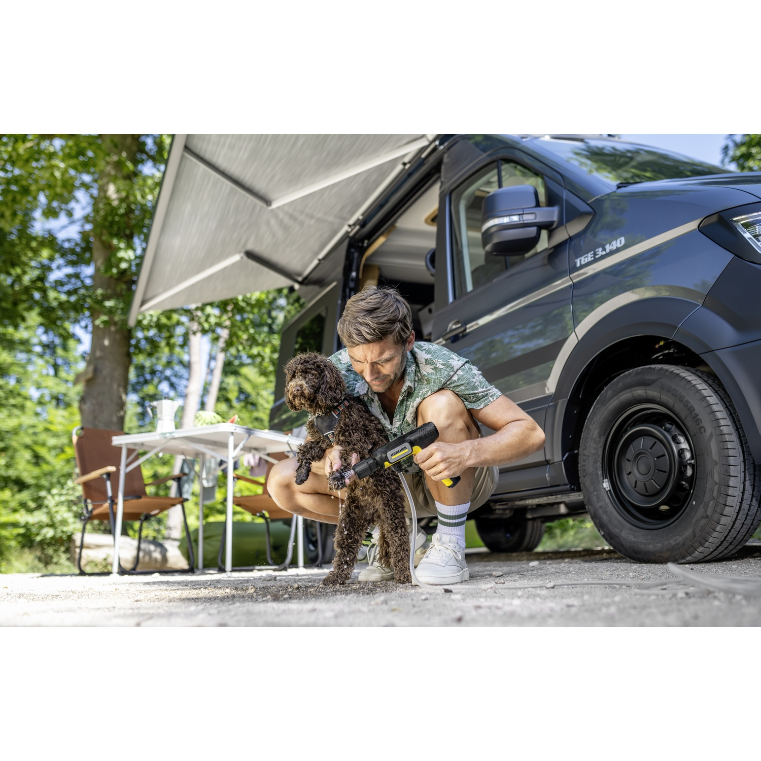 Uomo lava cane con dispositivo Karcher vicino a camper, tendalino esteso.