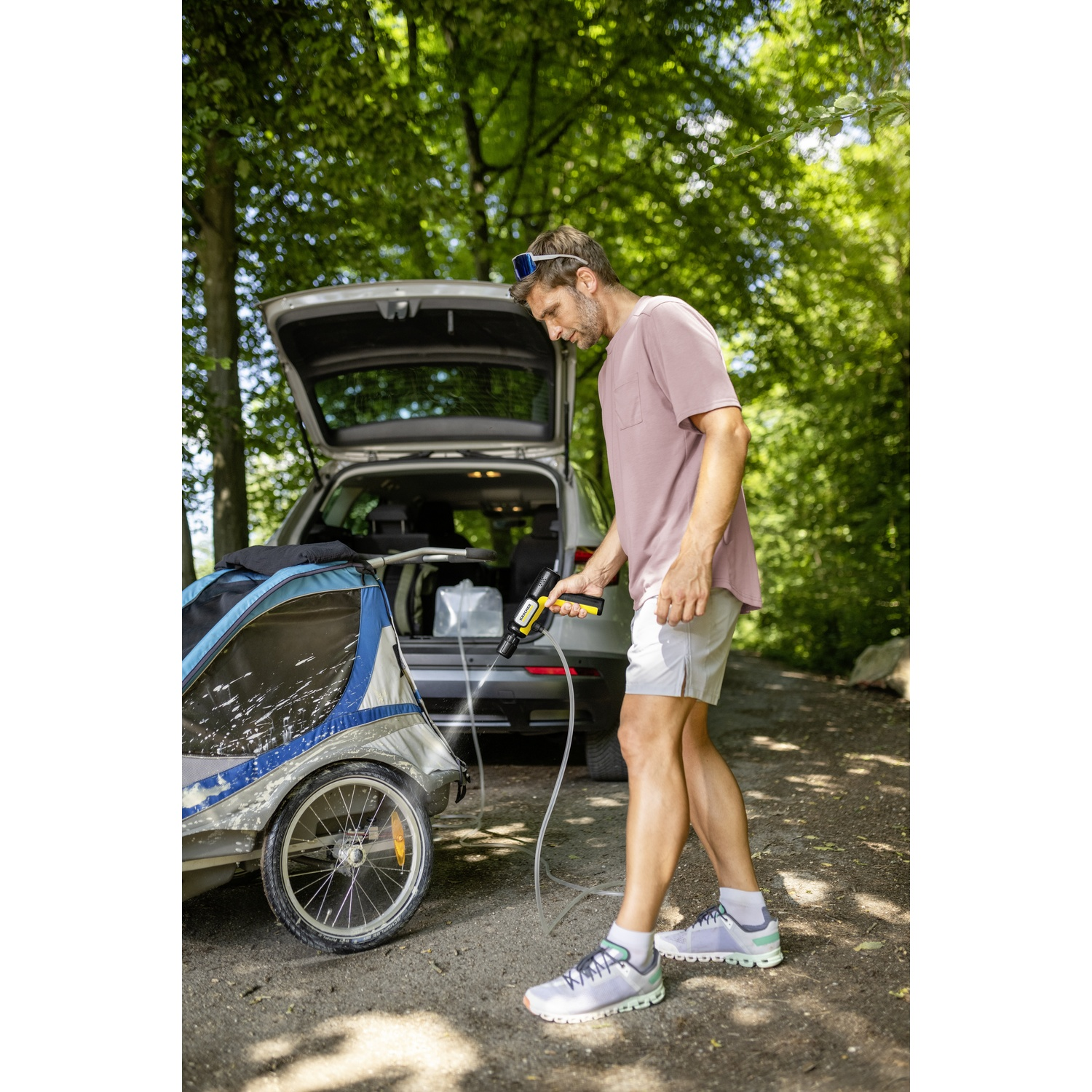 Uomo pulisce carrello bici con idropulitrice accanto ad auto.