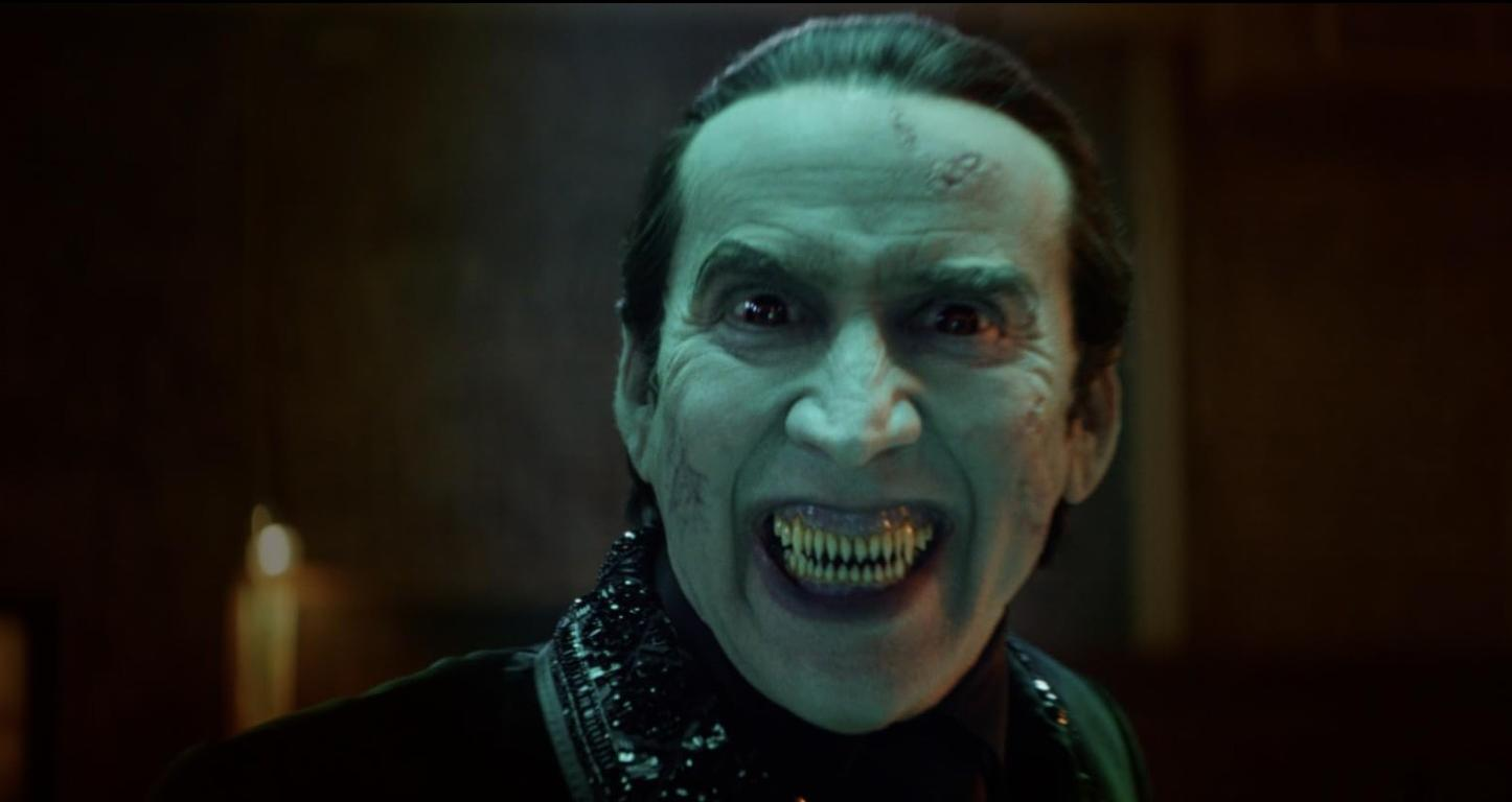 Ein Mann mit bleicher Haut und roten Augen lächelt mit spitzen Zähnen.