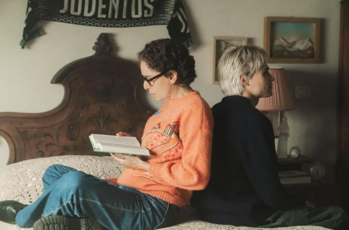 Zwei Personen sitzen auf einem Bett. Eine liest ein Buch, die andere schaut weg. Ein Juventus-Schal hängt darüber.