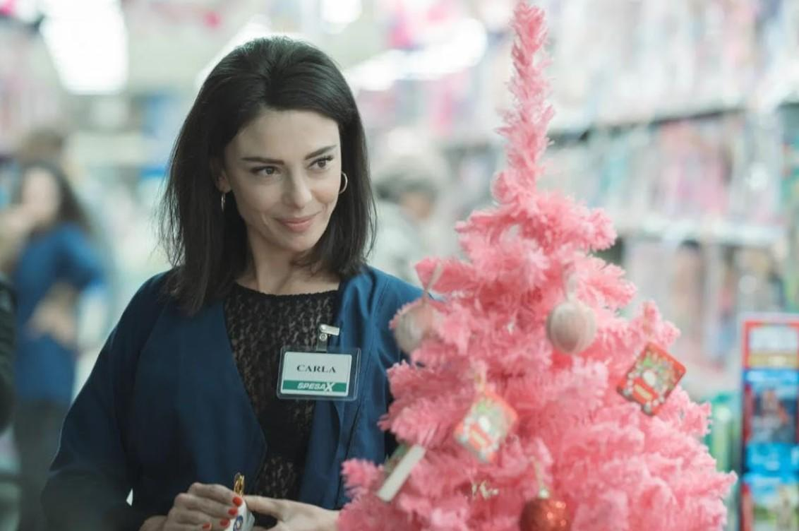 Eine Frau namens Carla lächelt in der Nähe eines pinken Weihnachtsbaums mit Schmuck in einem Geschäft.