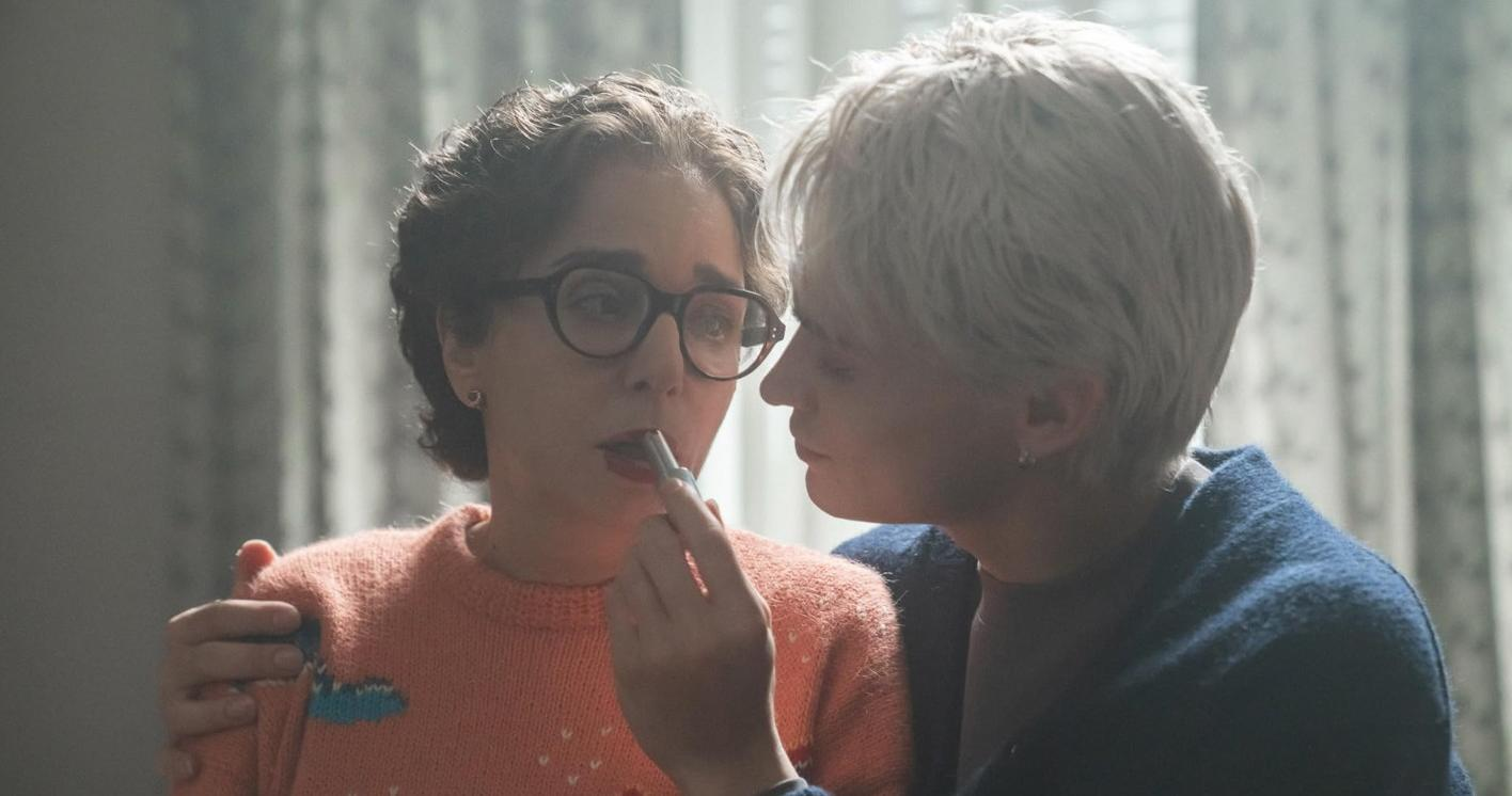 Eine Frau schminkt einer anderen Frau mit Brille die Lippen. Sanftes Licht.