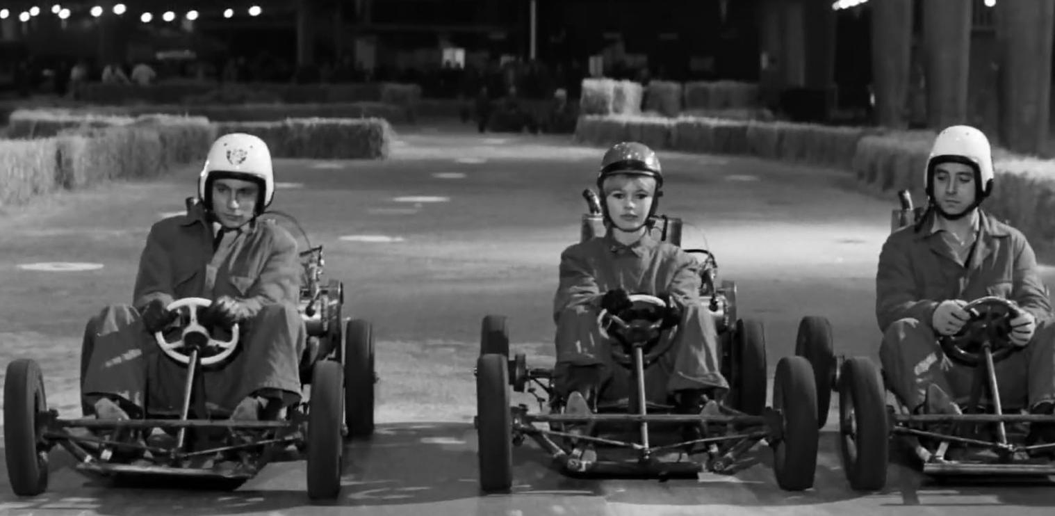 Drei Personen in Go-Karts auf einer Rennstrecke, im Freien bei Nacht.