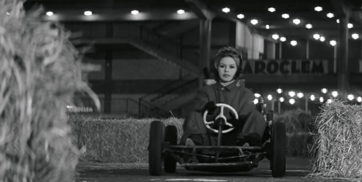 Eine Frau in einem Go-Kart fährt bei Nacht auf einer Strecke mit Heuballen und Lichtern.