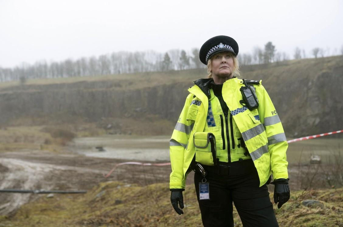 Polizistin in Warnweste und Mütze steht in felsiger Landschaft.