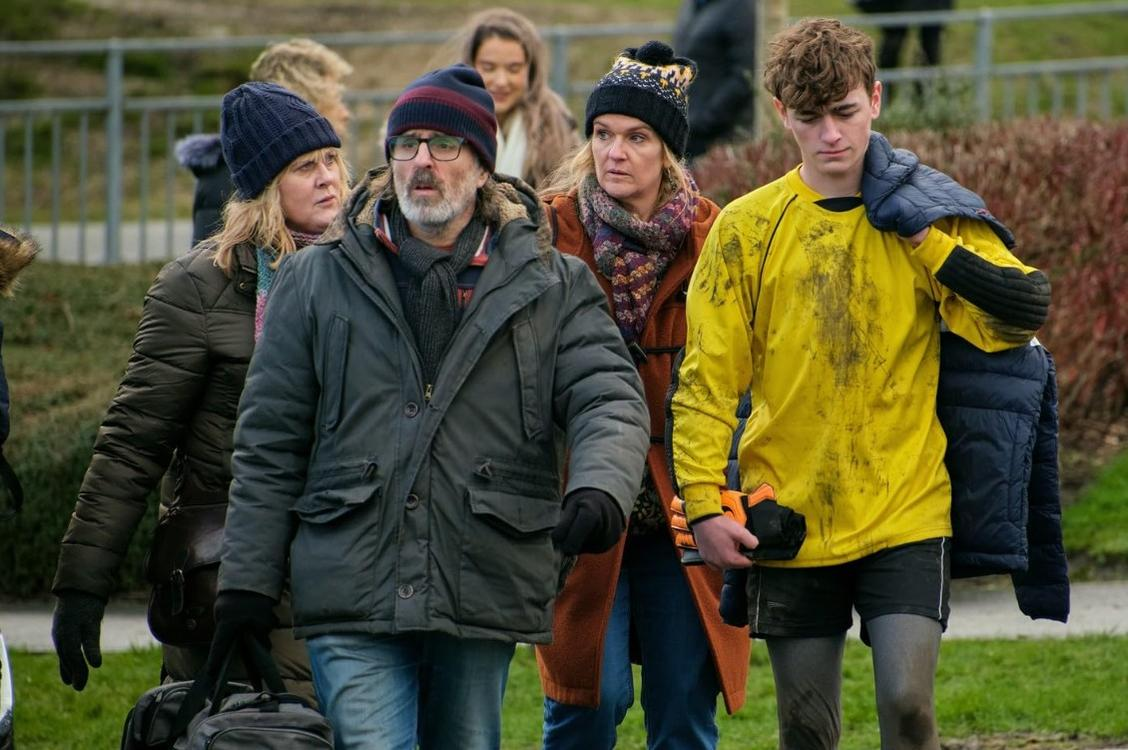 Eine Gruppe von Menschen geht auf einem Feld. Ein Junge trägt ein schmutziges gelbes Trikot.