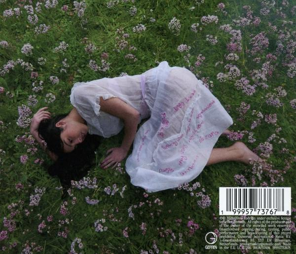 Eine Frau in einem weißen Kleid liegt auf einer Wiese voller Blumen.