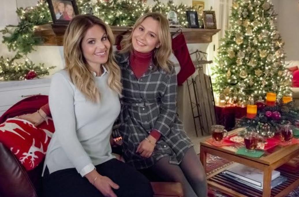 Zwei Frauen sitzen vor einem Kamin mit Weihnachtsdekoration, einem Weihnachtsbaum und einem Tisch.