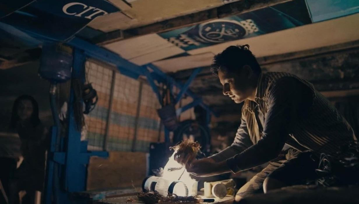 Ein Mann kniet und arbeitet an einer Lampe. Eine Frau steht im Hintergrund.