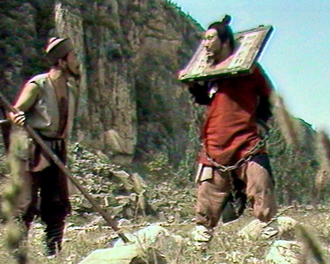 Ein Mann mit einem Holzgefängnis am Hals und Ketten steht vor einem Berg.