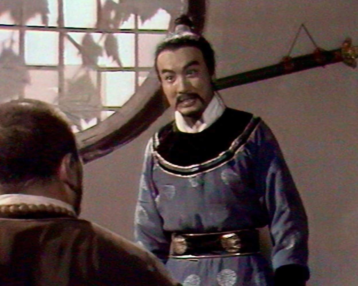 Ein Mann in blauer traditioneller asiatischer Kleidung mit schwarzem Kragen spricht zu einem anderen Mann.