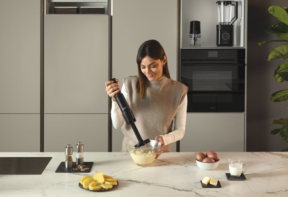 Kadın, siyah el blenderı ile bir kapta patates püresi yapıyor. Mutfak tezgahı.