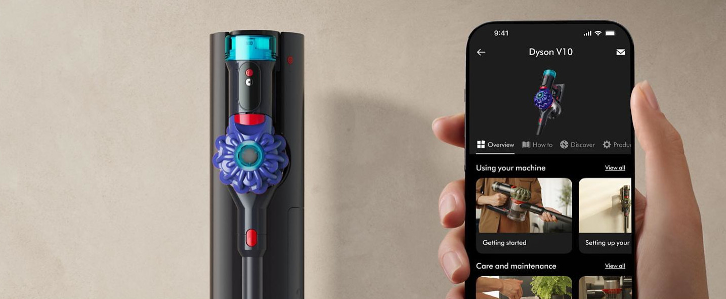 Odkurzacz Dyson V10 w stacji ładującej obok smartfona wyświetlającego aplikację Dyson.