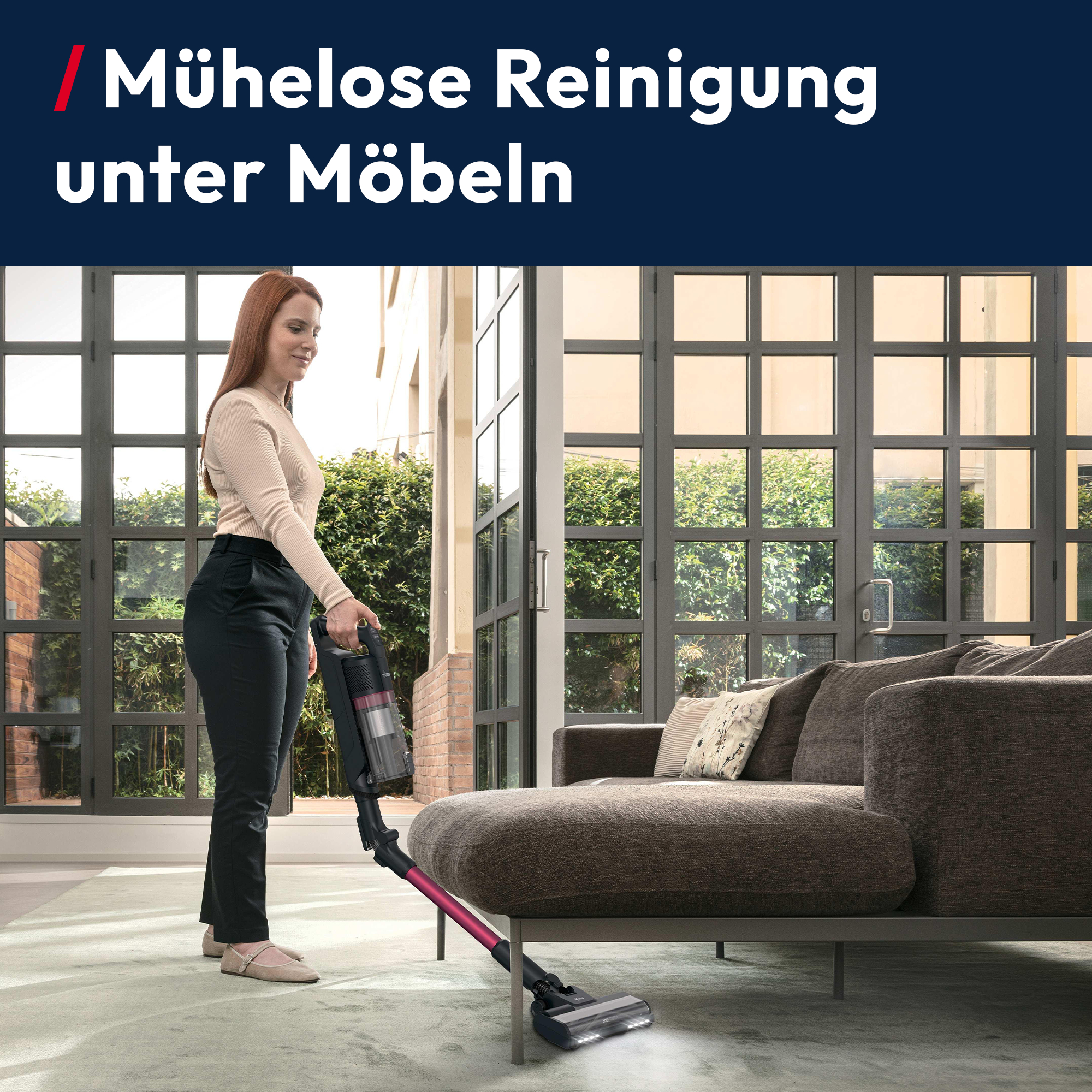Eine Frau saugt unter einem Sofa mit einem kabellosen Staubsauger.