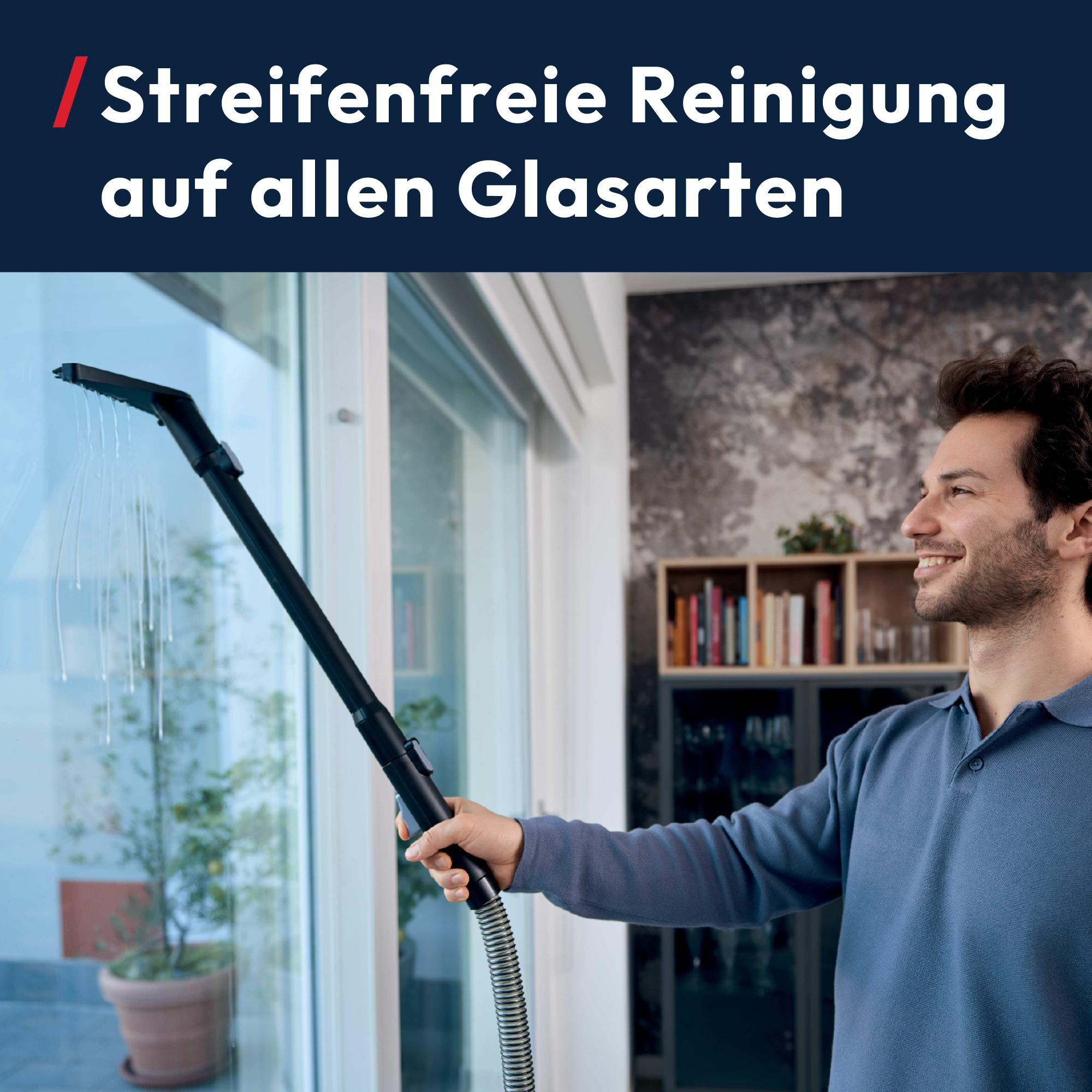 Mann reinigt Fenster mit Sprühgerät. Innenraum mit Bücherregal.