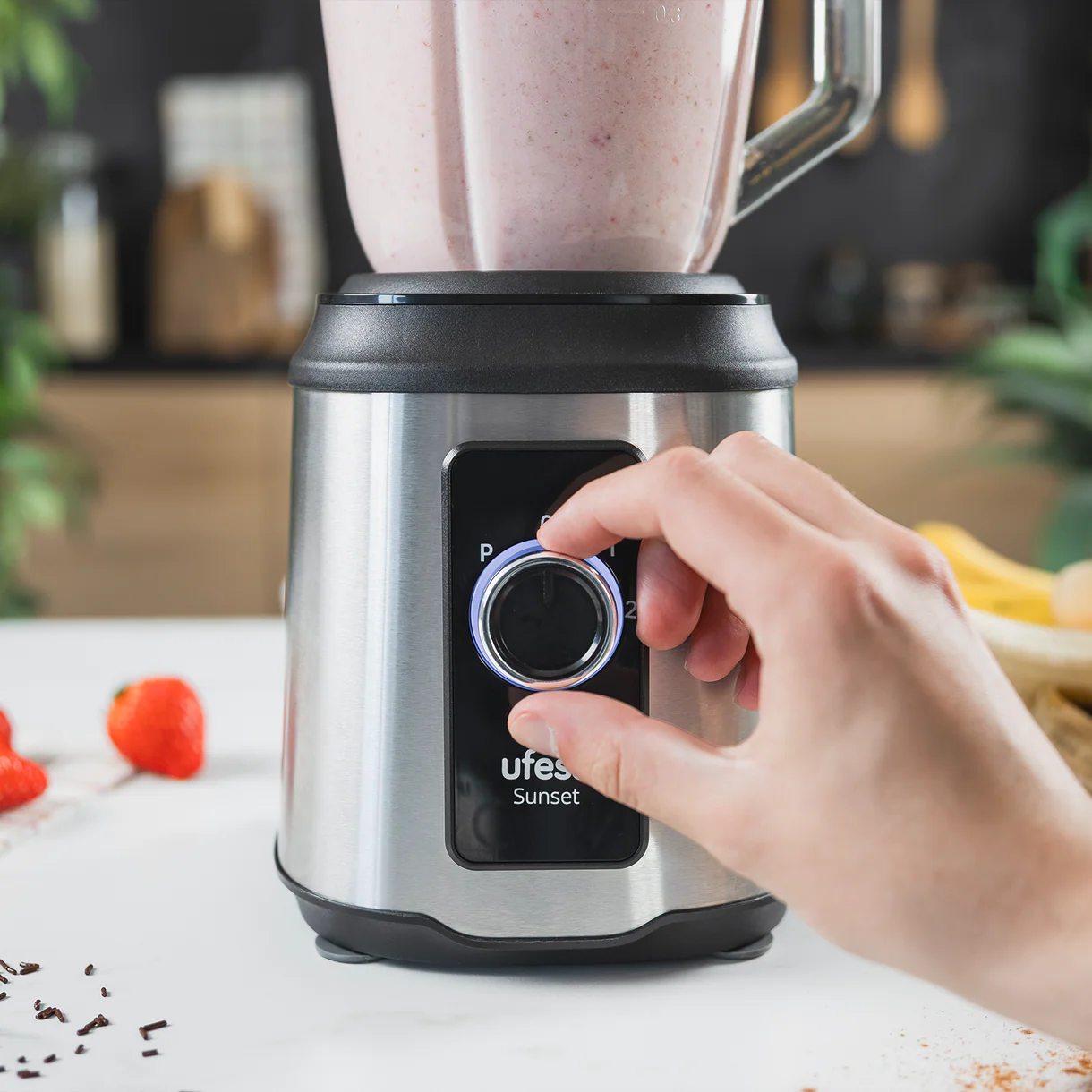 Una mano gira el dial de una licuadora con relleno de batido de fresa.