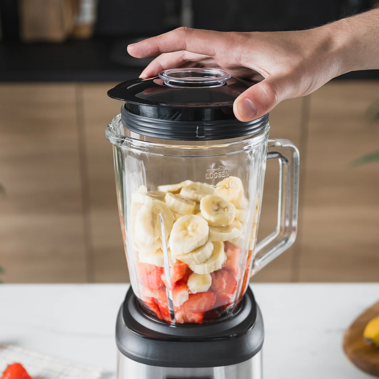 Una mano cierra la tapa de una licuadora con fresas y plátanos.