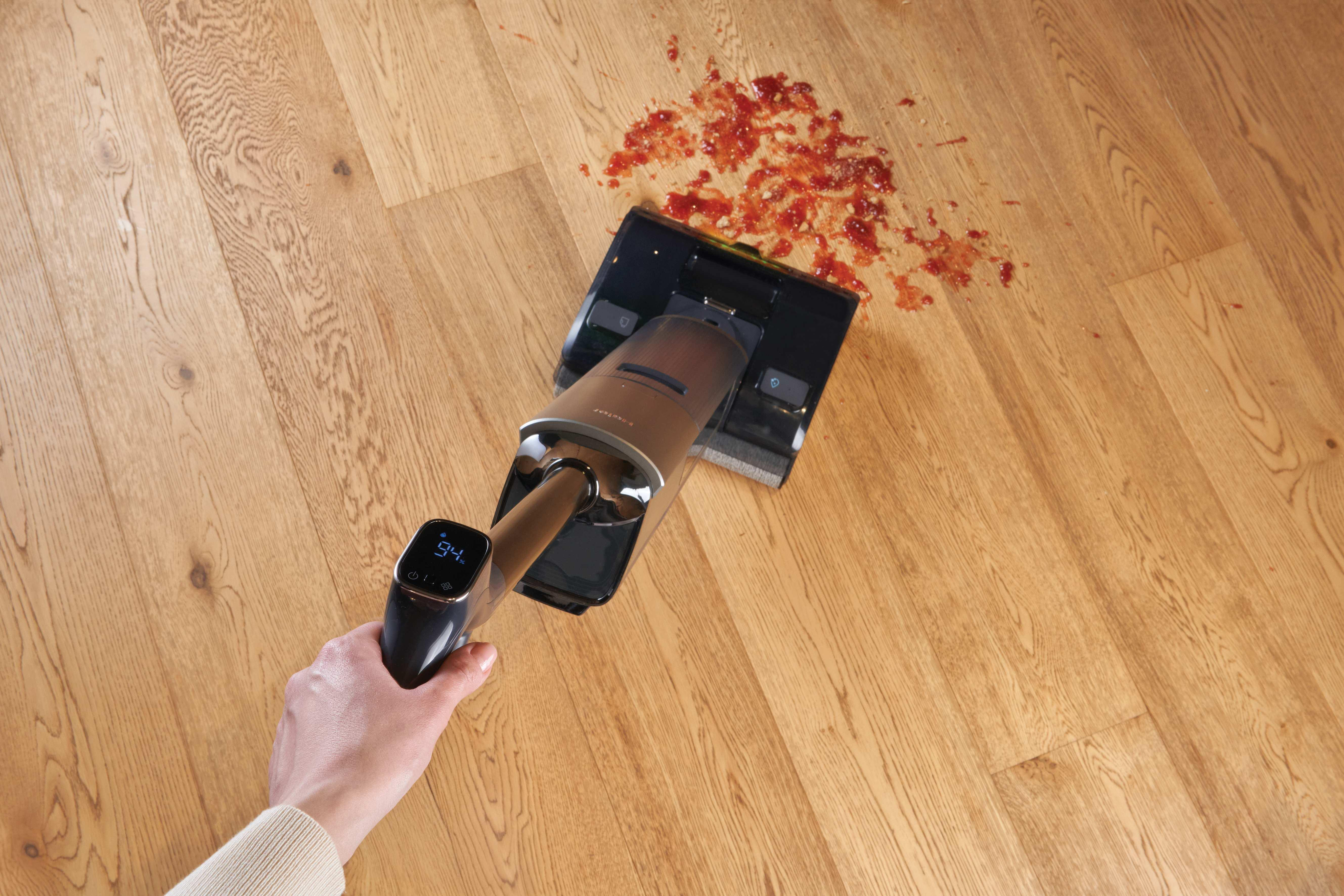 Ein Handstaubsauger reinigt rote Soße auf einem Holzboden.