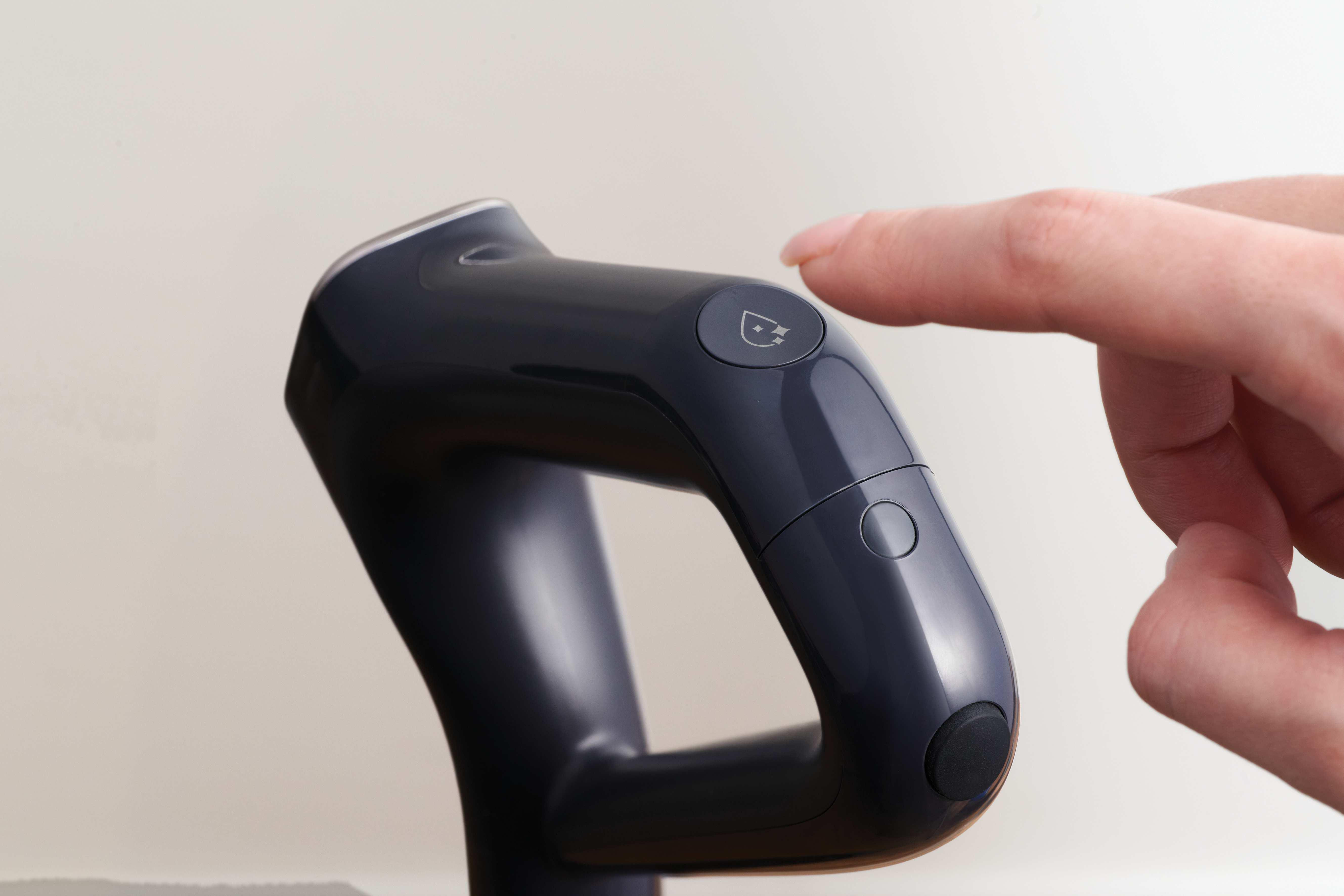 Ein Finger drückt auf einen Knopf mit einem Symbol auf einem dunklen Griff.