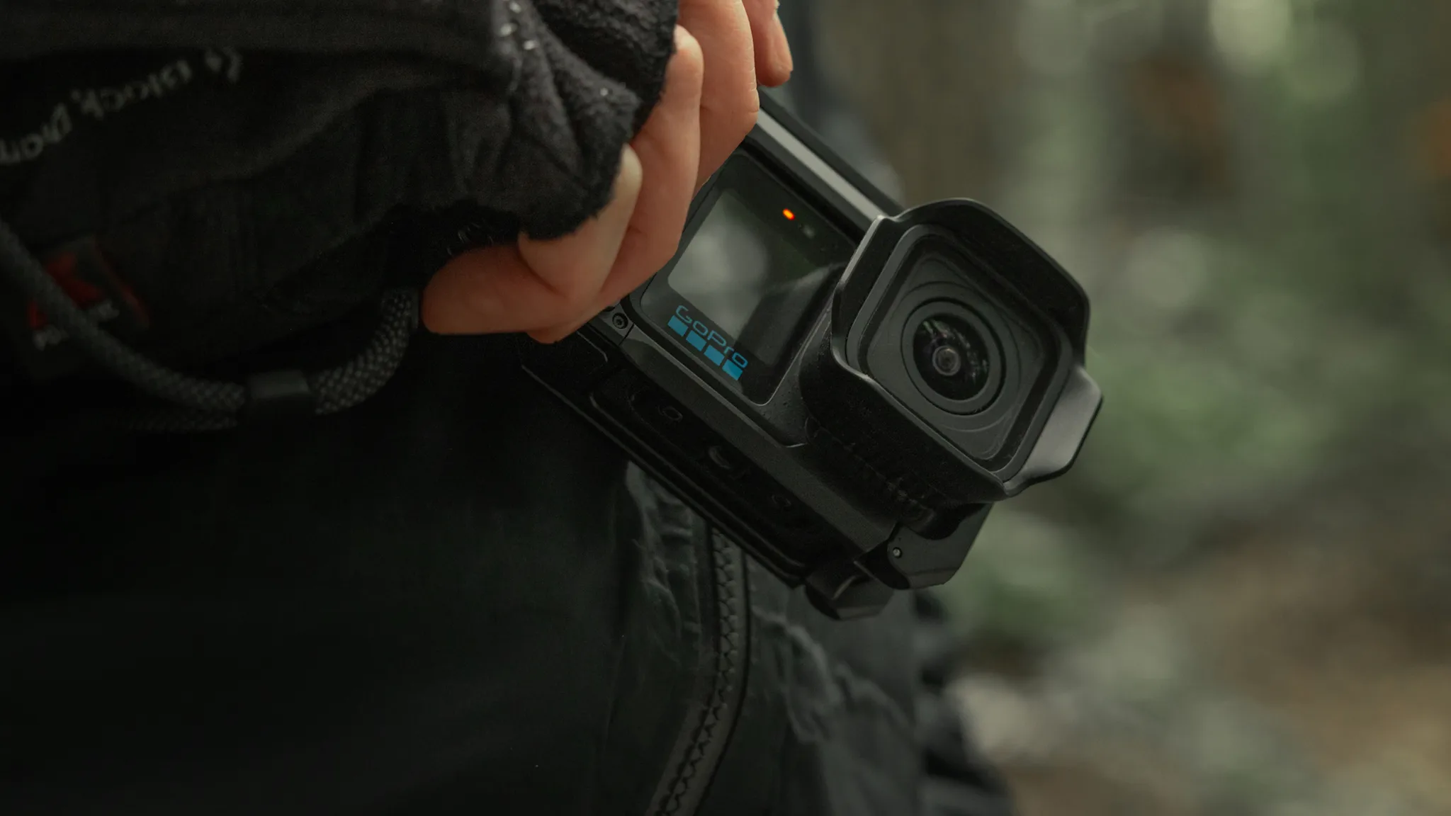 Egy GoPro kamerát tartó kéz közelről, elmosódott háttérrel.