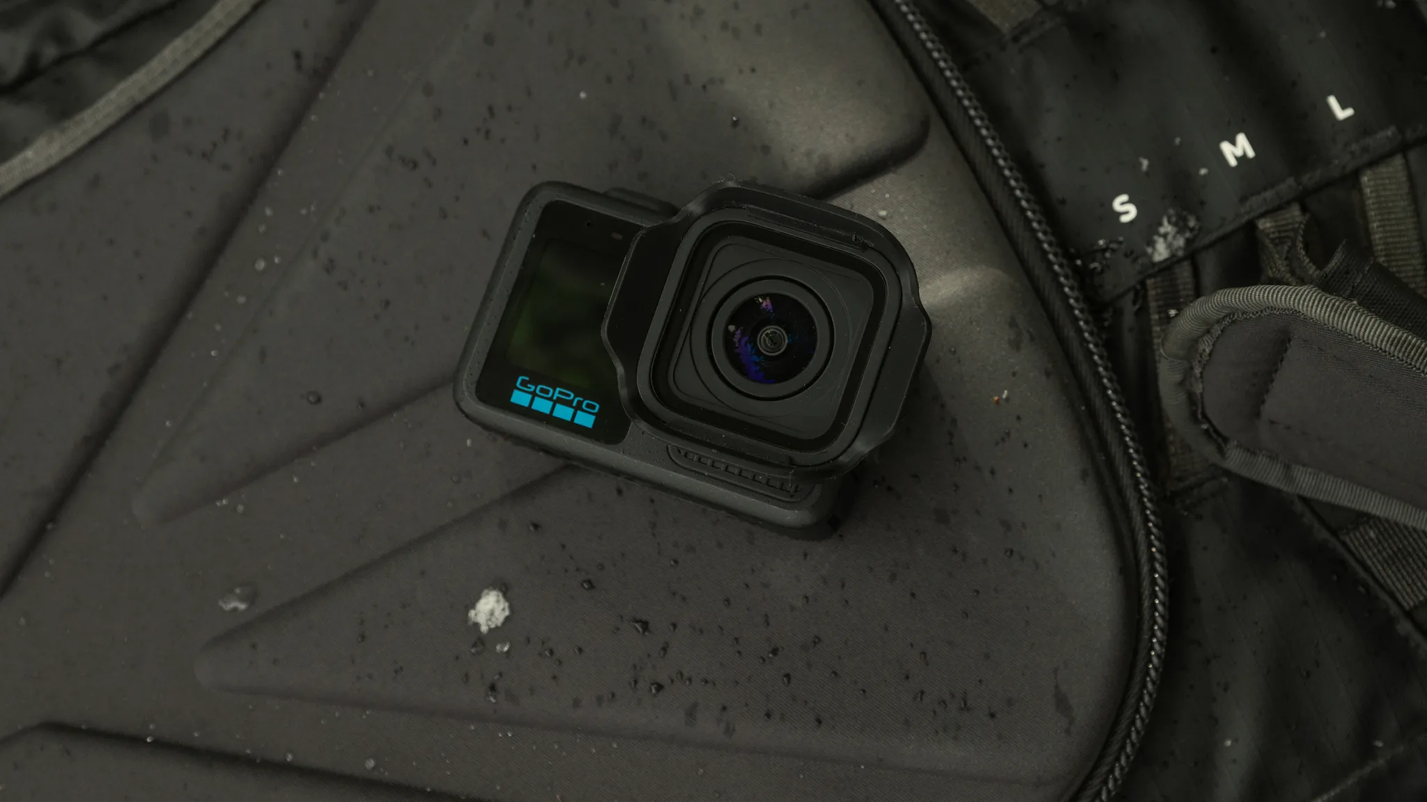 Egy fekete GoPro kamera egy vizes, sötét, cipzáras anyagon pihen.
