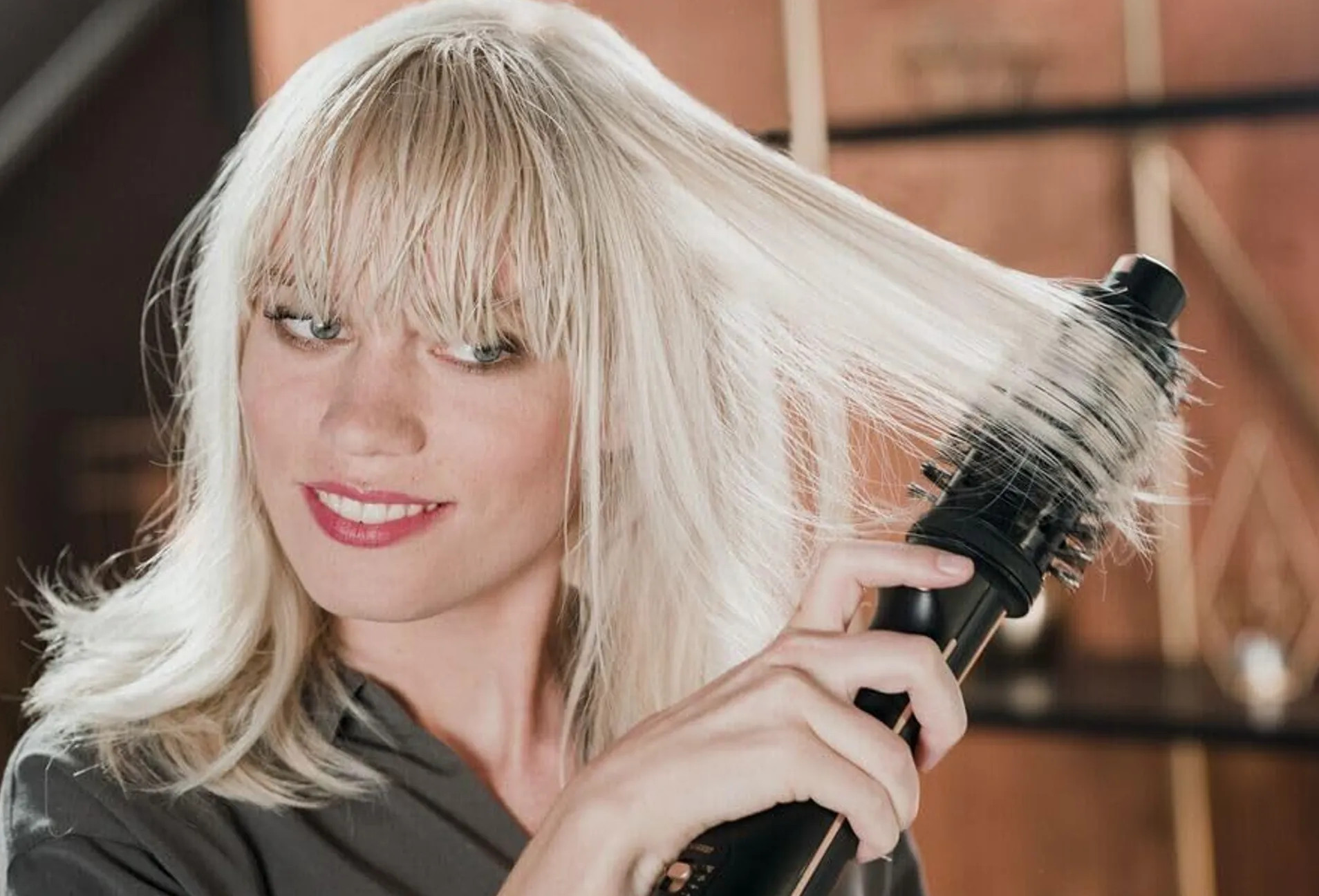 Kobieta z blond włosami suszy włosy okrągłą szczotką i suszarką.