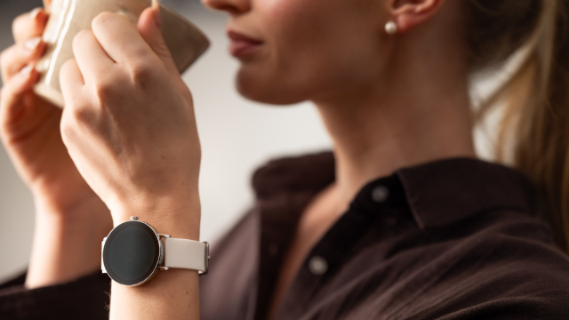 Una donna beve da una tazza, indossa uno smartwatch con cinturino bianco.