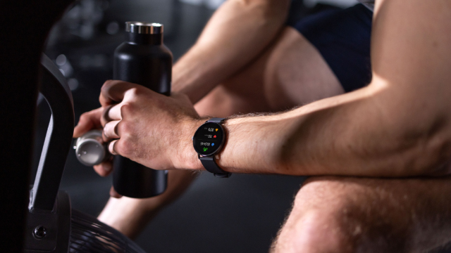 Uomo con smartwatch tiene bottiglia d'acqua nera, attrezzo fitness in primo piano.