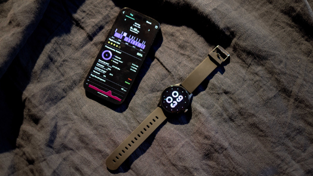 Uno smartwatch e un telefono mostrano dati sul sonno su tessuto scuro e rugoso.