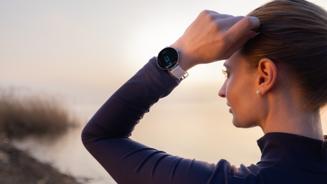 Donna con smartwatch al polso guarda fuori mentre si sistema i capelli.