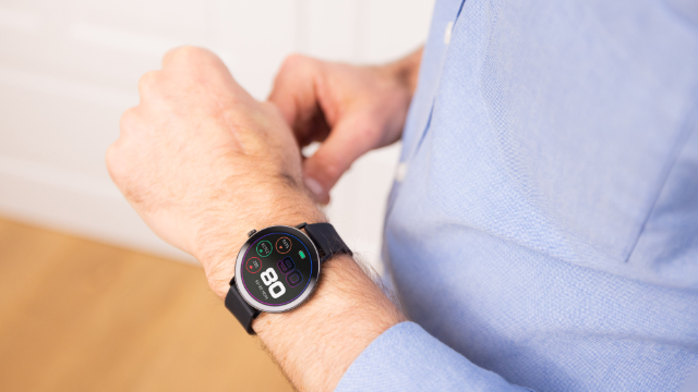 Uomo con camicia blu e smartwatch che mostra la frequenza cardiaca.