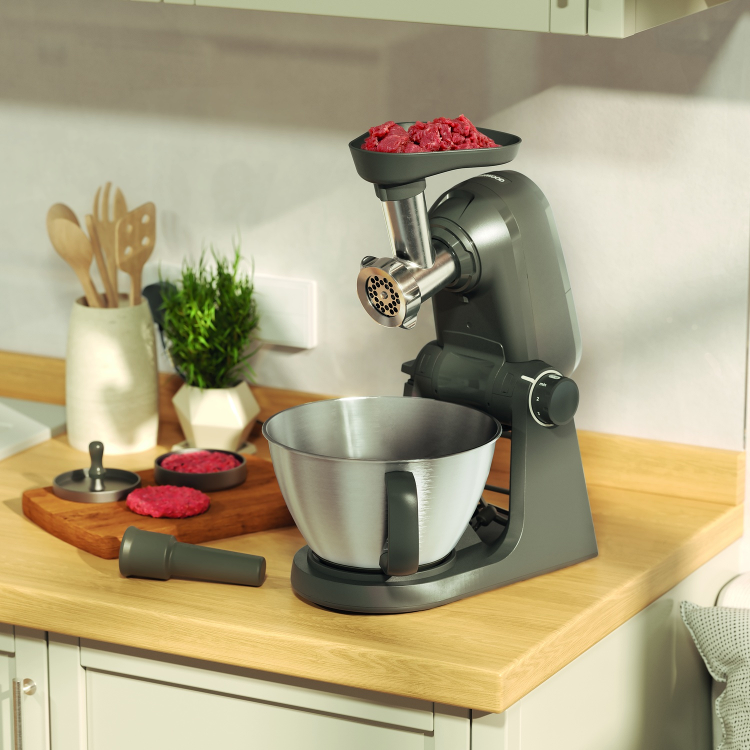 A dark grey meat grinder attachment is on a stand mixer with a bowl and raw meat.