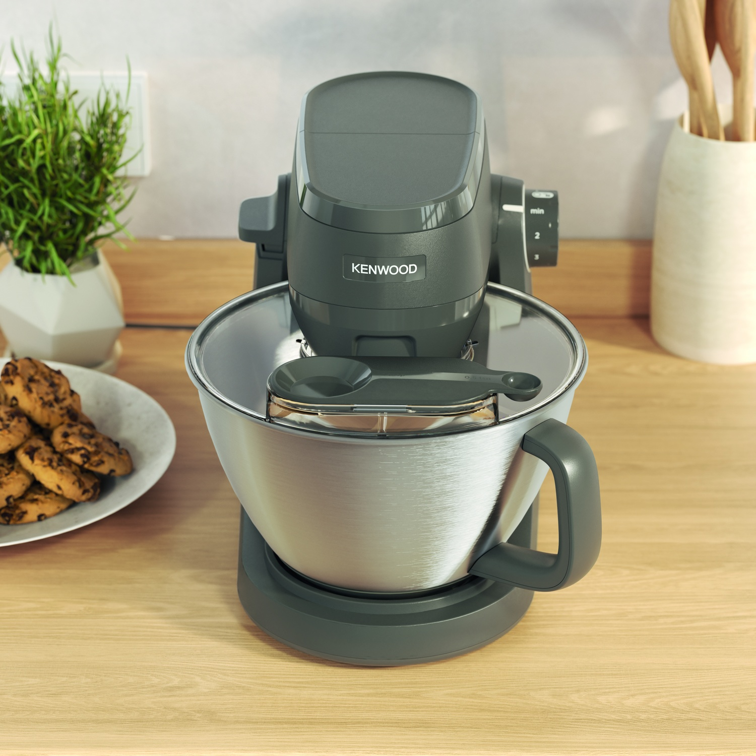 Grey Kenwood stand mixer with stainless steel bowl, next to a plate of cookies.