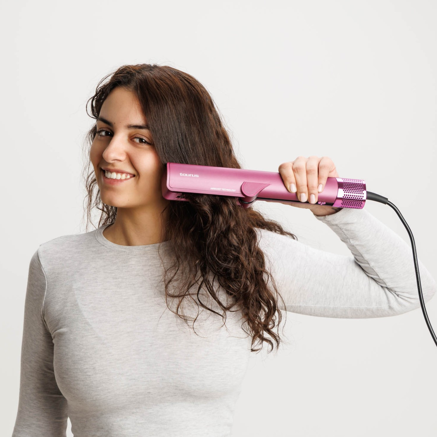 Mujer con pelo castaño usa una plancha de pelo rosa.