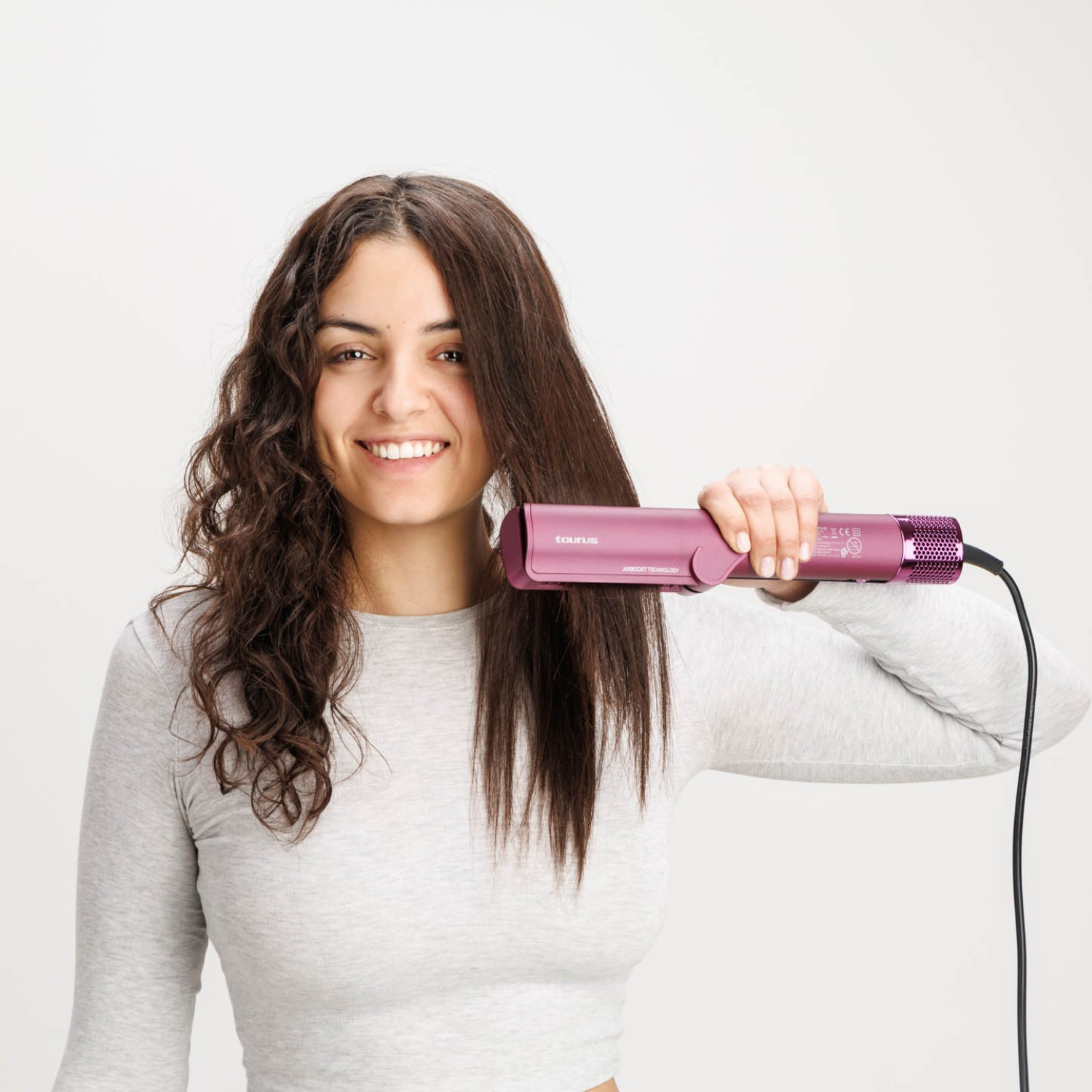 Una mujer con pelo castaño largo sostiene una plancha morada.