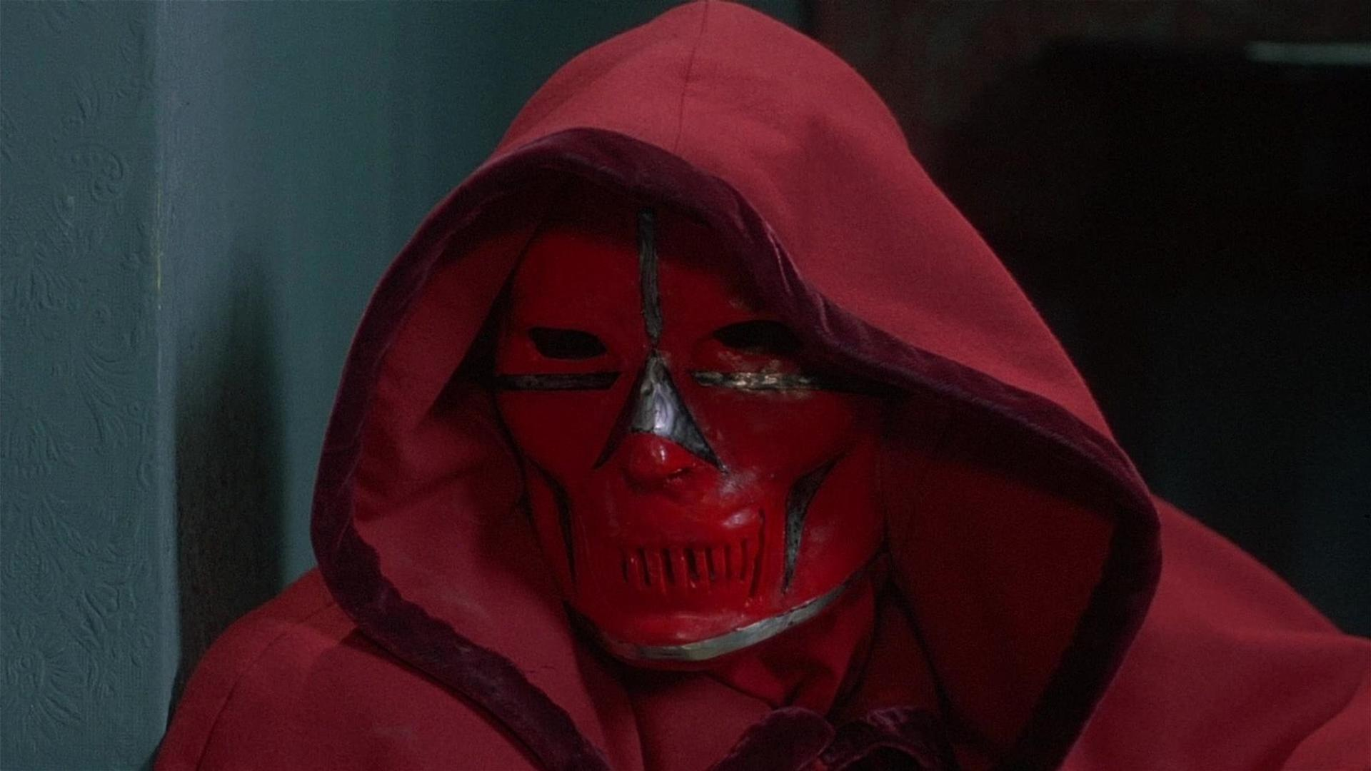 Eine Person in einer roten Robe mit Kapuze trägt eine rote Maske.