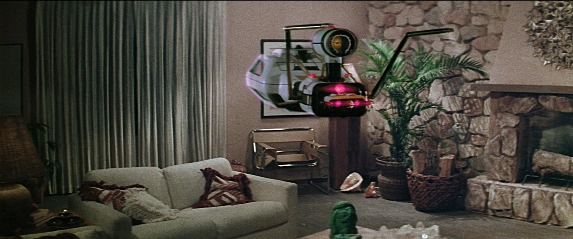 Ein futuristisches Gerät schwebt über einem Sofa in einem Wohnzimmer mit Kamin.