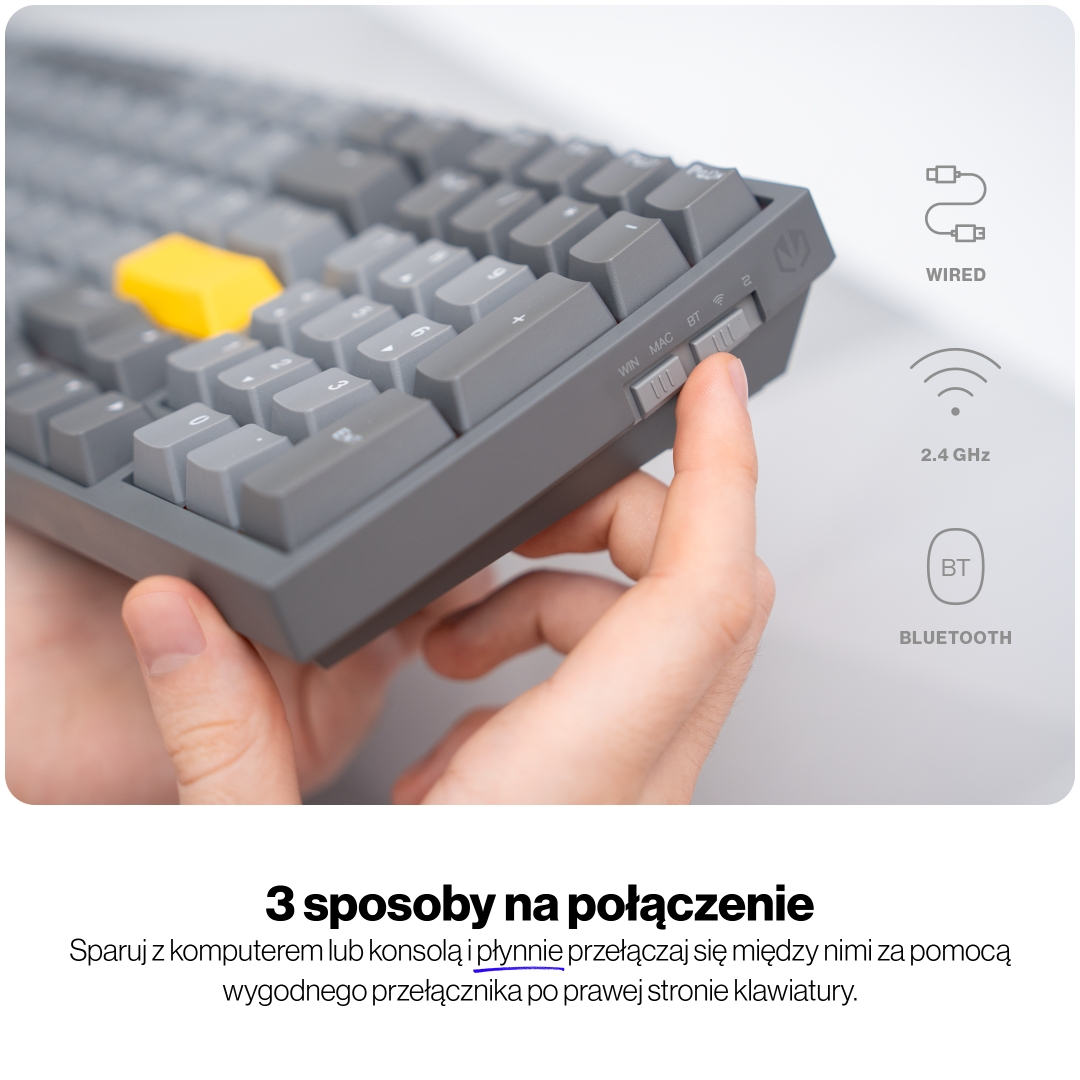 Szara klawiatura z żółtym klawiszem, palec przełącza WIN, MAC, BT.