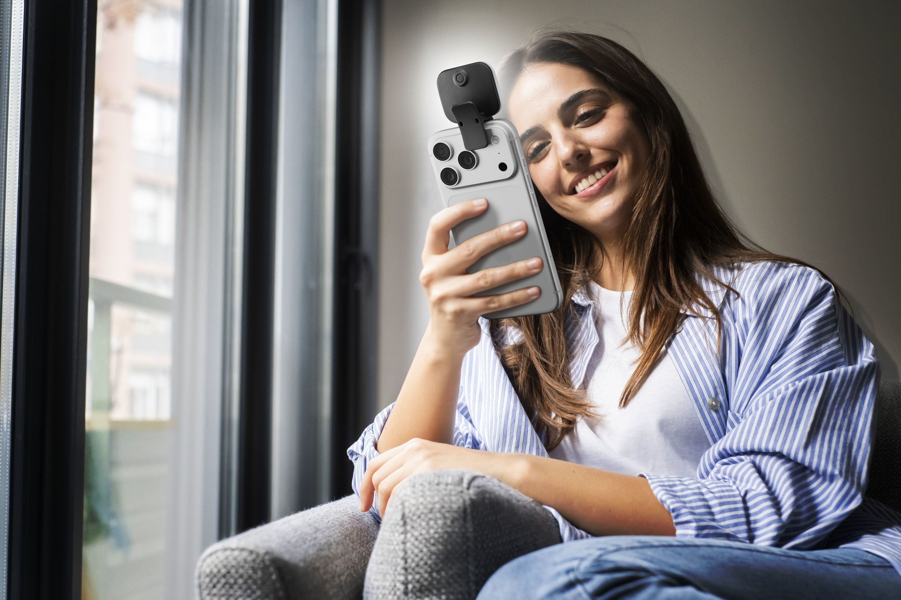 Kadın, üzerine takılı küçük bir kamerayla telefonu tutarken gülümsüyor.