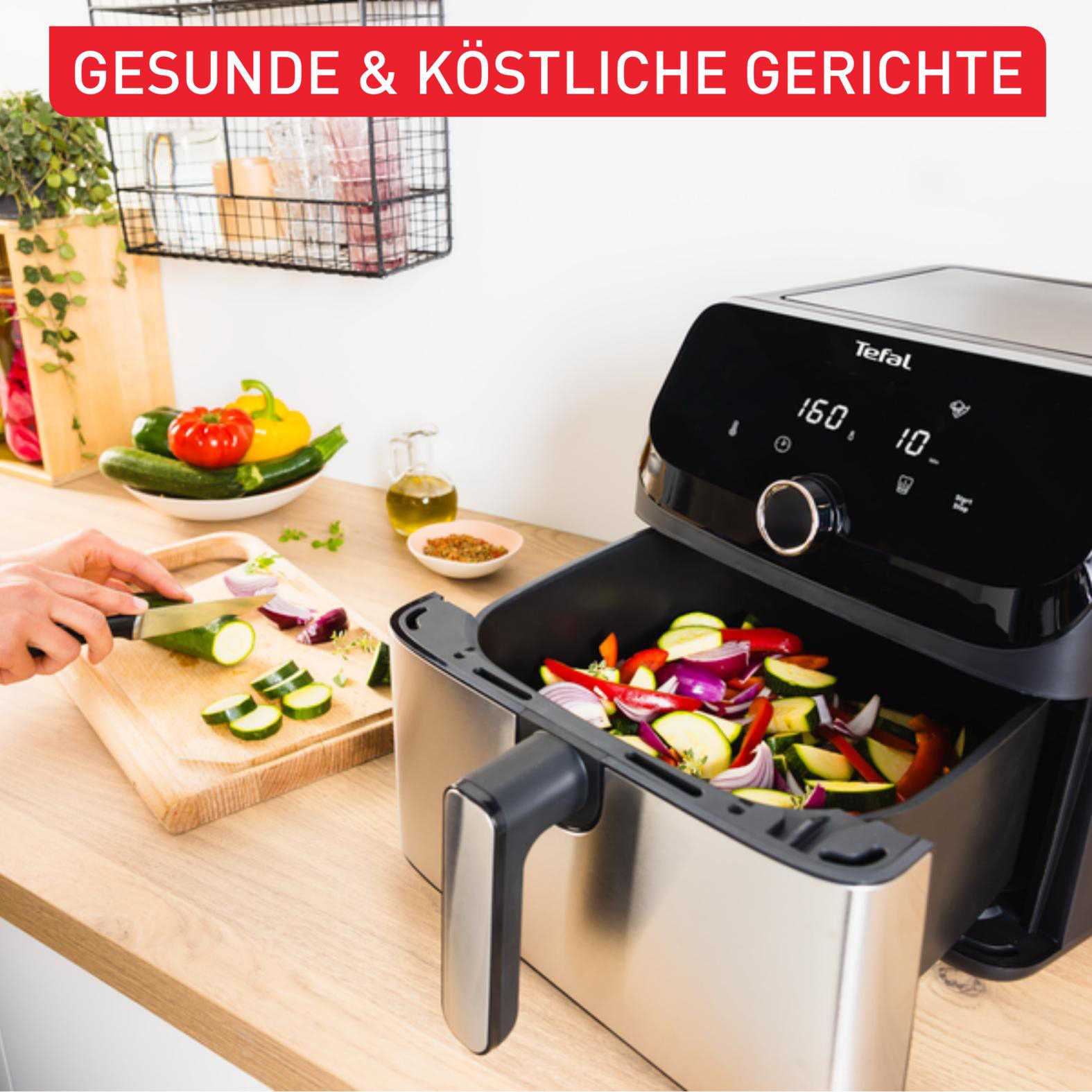 Eine Person schneidet Zucchini; daneben eine Heißluftfritteuse mit Gemüse.
