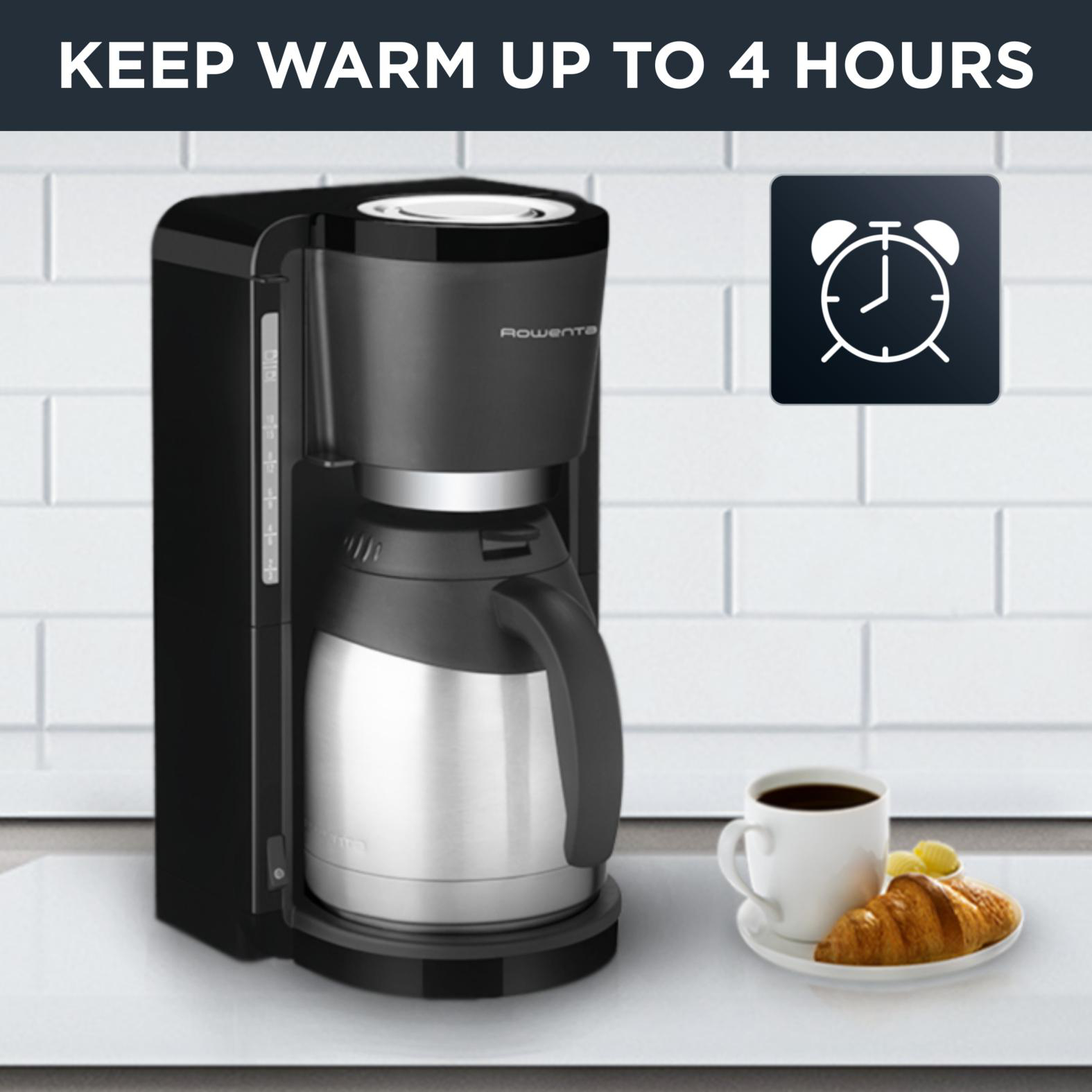 Eine schwarze Kaffeemaschine mit Thermoskanne neben einer Tasse Kaffee und einem Croissant.