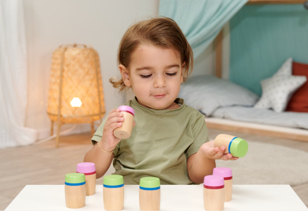 Ein kleines Kind spielt mit Holzspielzeug. Es hält zwei Becher in den Händen.