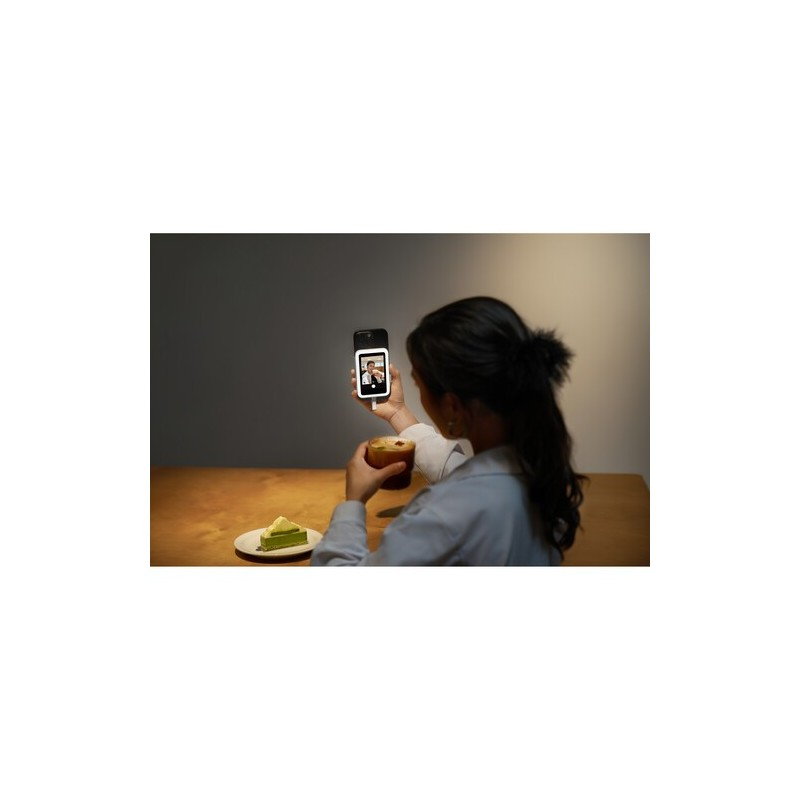 Una mujer sostiene un teléfono mostrando videollamada y bebe de una taza.